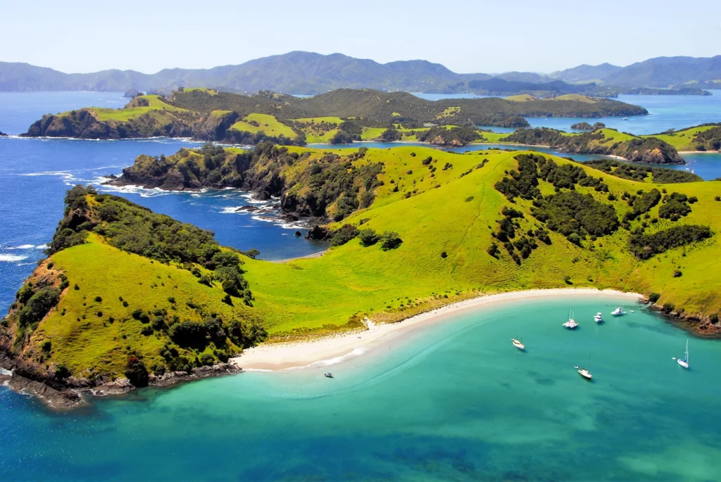 Luxury yacht sailing along New Zealand’s coastline, with dramatic fjords, lush hills, and clear blue waters in the background