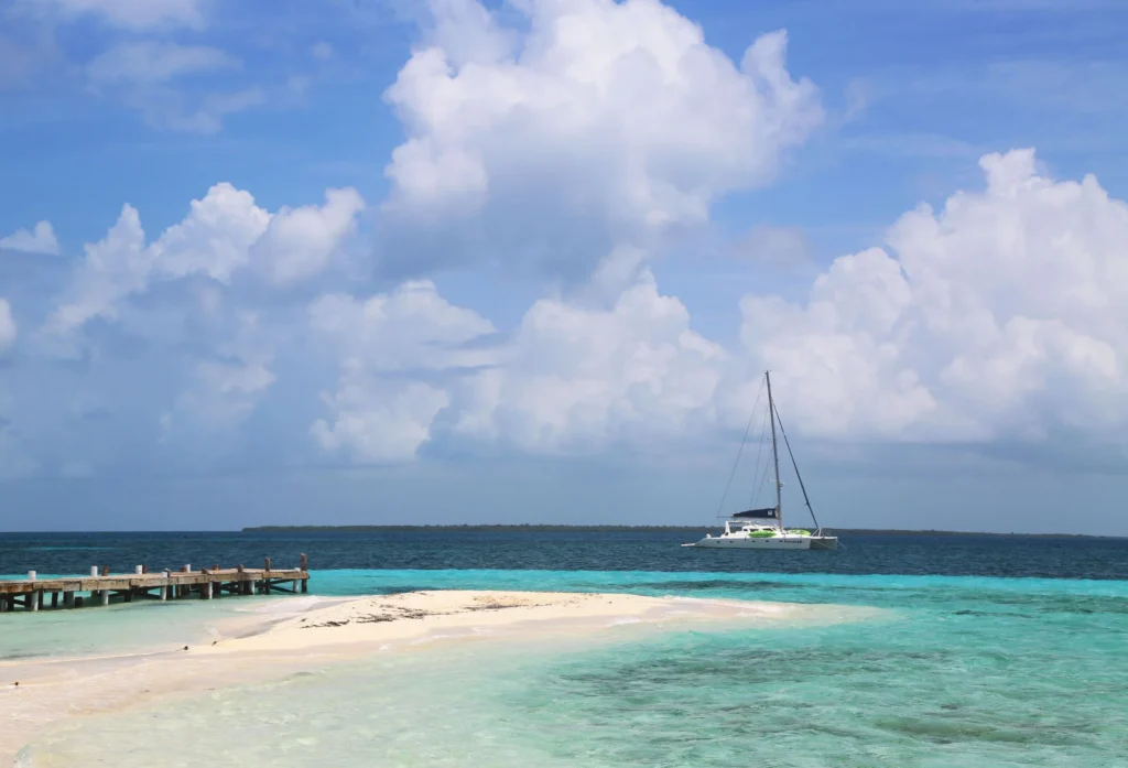 Luxury yacht sailing near the Belize Barrier Reef, with crystal-clear turquoise waters, vibrant coral reefs, and a white sandy beach in the background