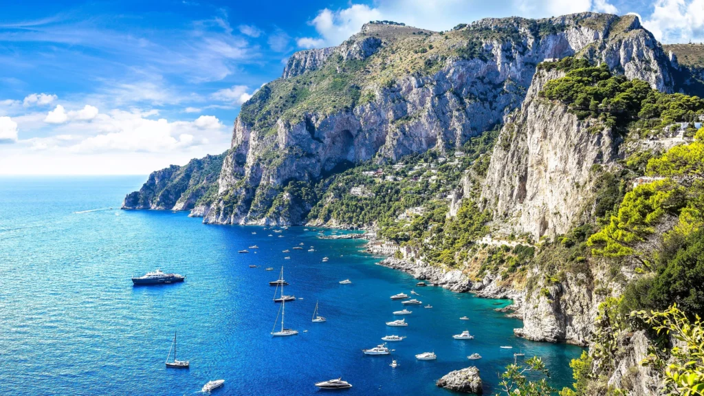 Luxury yacht anchored near Capri, Italy, with the iconic Faraglioni rock formations, turquoise waters, and lush green cliffs in the background