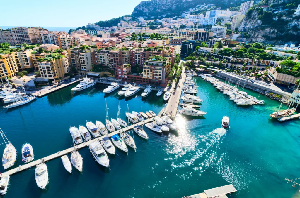 Luxury yacht anchored in Port Hercules, Monaco, with the Monte Carlo skyline, turquoise waters, and luxurious waterfront in the background