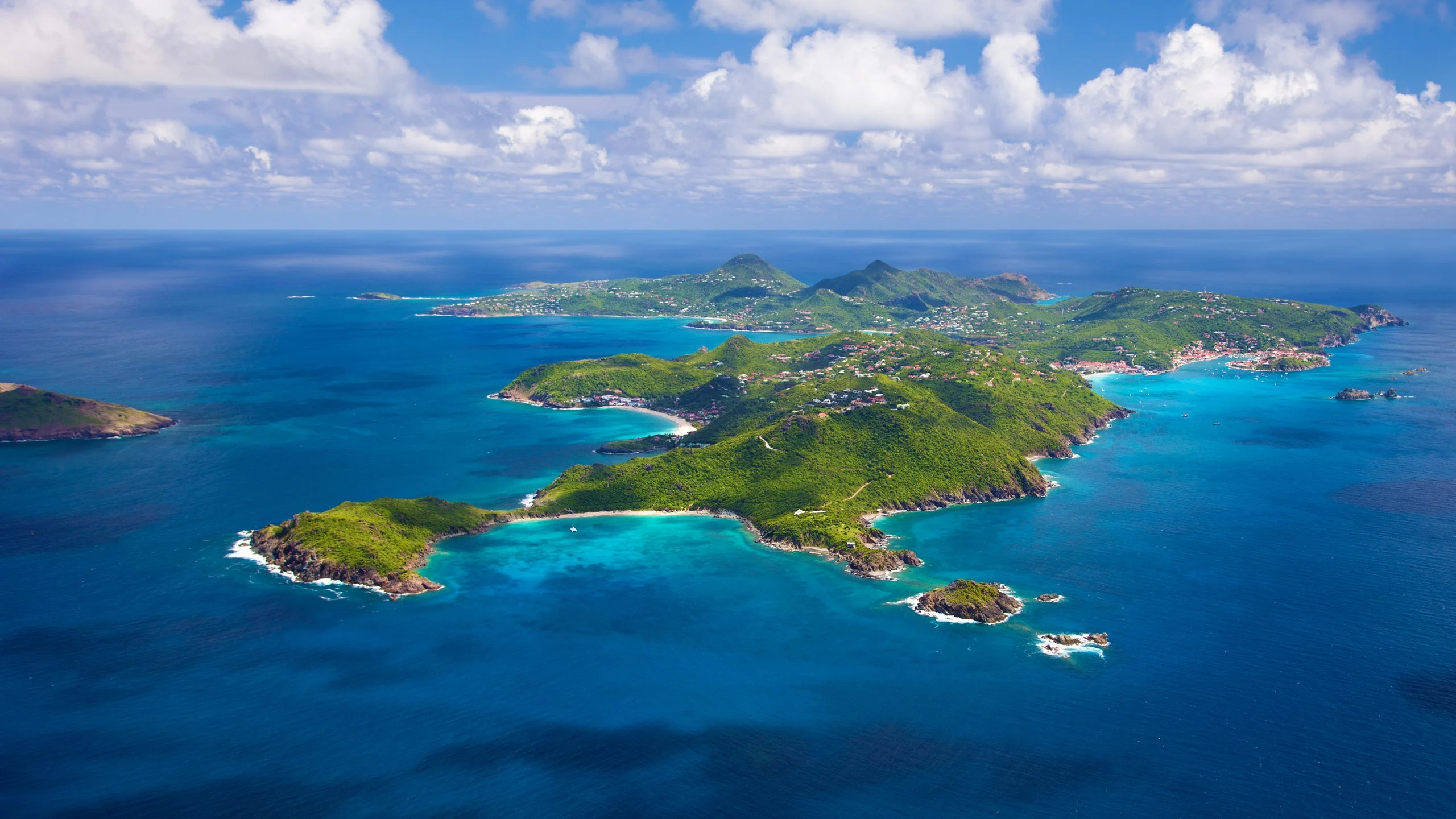 Luxury yacht anchored near St. Barths, with turquoise waters, white-sand beaches, and upscale beachfront villas nestled along the hills.
