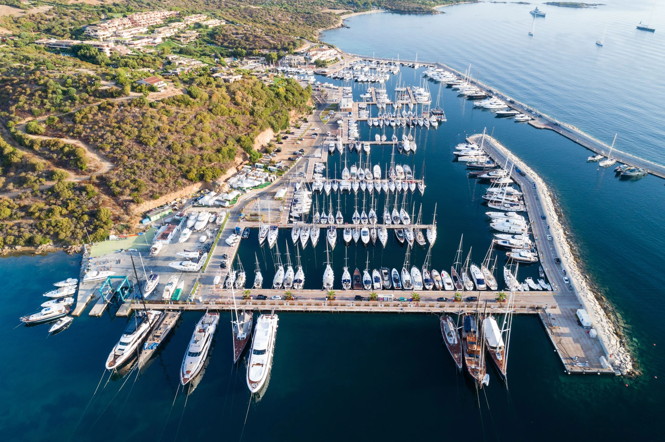 Luxury yacht anchored in Portisco Marina, Sardinia, Italy, with the iconic waterfront, turquoise waters, and lush green hills in the background