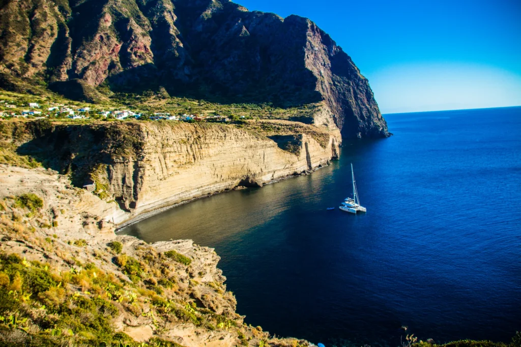Luxury yacht anchored near the coastline of Cefalù, Sicily, Italy, with the iconic Cefalù Cathedral, golden sandy beaches, and turquoise waters in the background