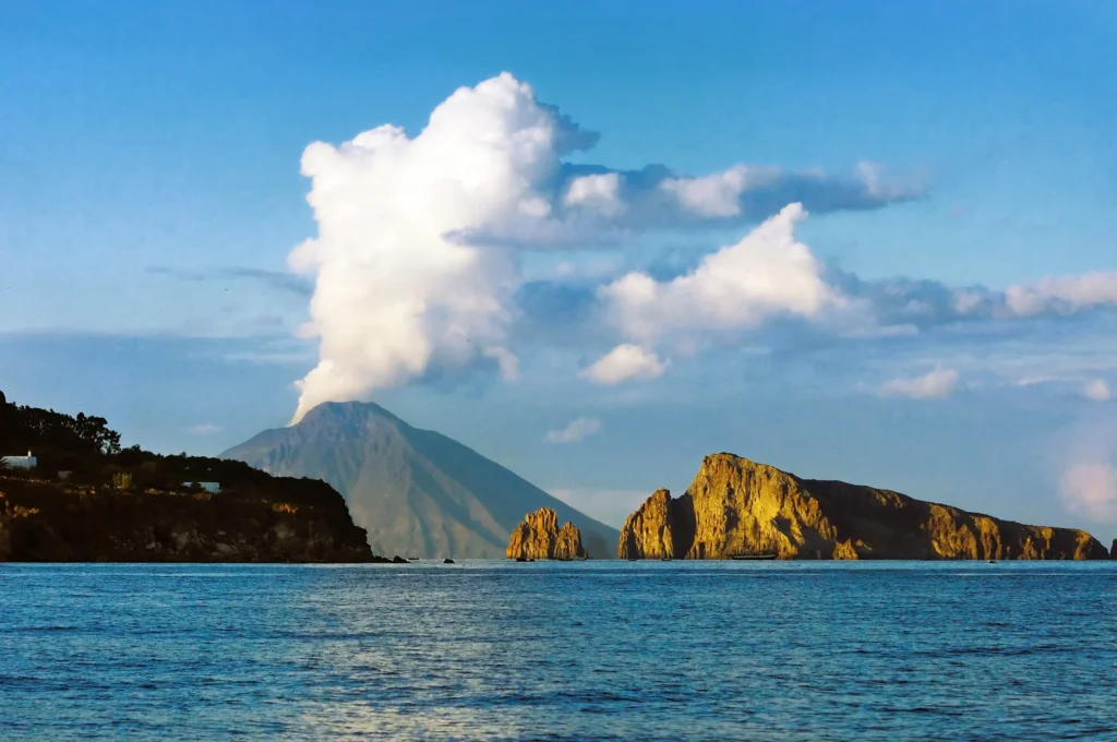 Luxury yacht anchored near the coastline of Stromboli, Sicily, Italy, with the iconic Stromboli volcano, black sandy beaches, and turquoise waters in the background