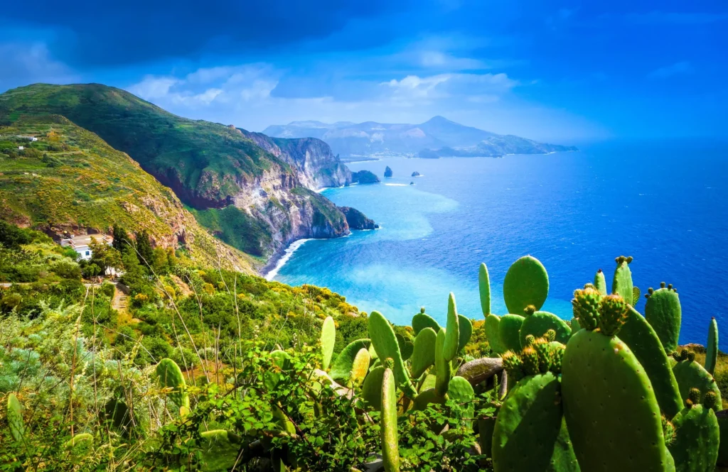 Luxury yacht anchored near the coastline of Lipari, Sicily, Italy, with the iconic Lipari Castle, turquoise waters, and lush green hills in the background.