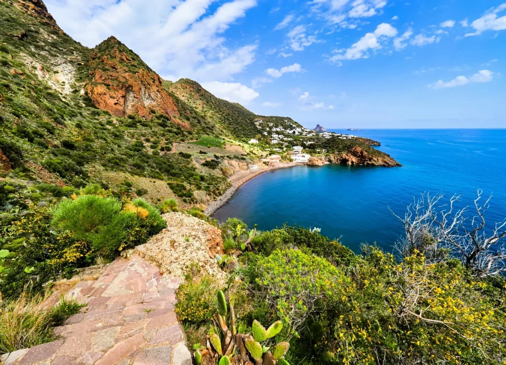 Luxury yacht anchored near the coastline of Panarea, Sicily, Italy, with whitewashed houses, turquoise waters, and dramatic volcanic landscapes in the background.