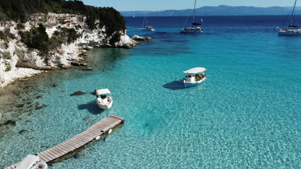 Luxury yacht cruising near Paxos, Greece, with crystal-clear Ionian Sea waters, lush landscapes, and charming island scenery with distant views of Corfu.