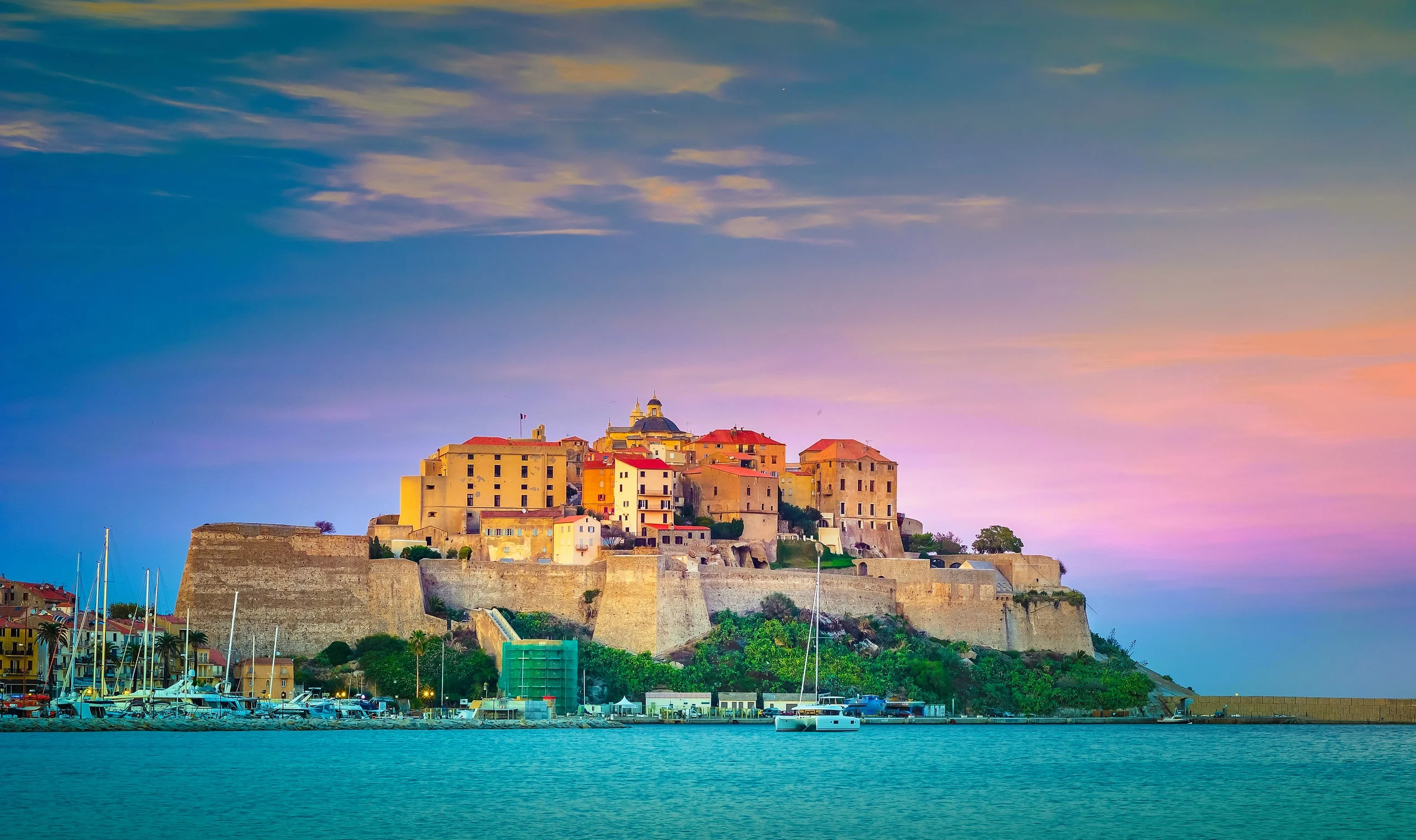 Luxury yacht cruising near Calvi, Corsica, featuring the iconic Calvi Citadel, dramatic coastal cliffs, and sparkling Mediterranean waters