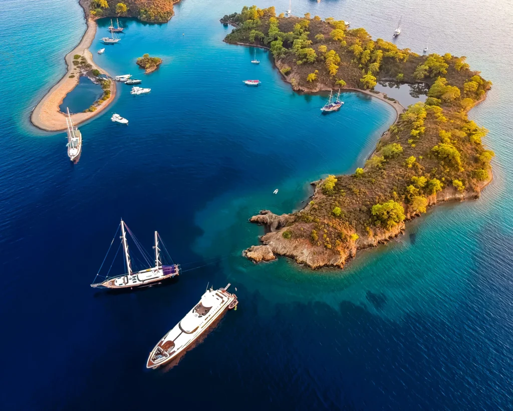 Luxury yacht cruising near Fethiye, Turkey, with crystal-clear turquoise waters, rugged coastline, and a charming marina.