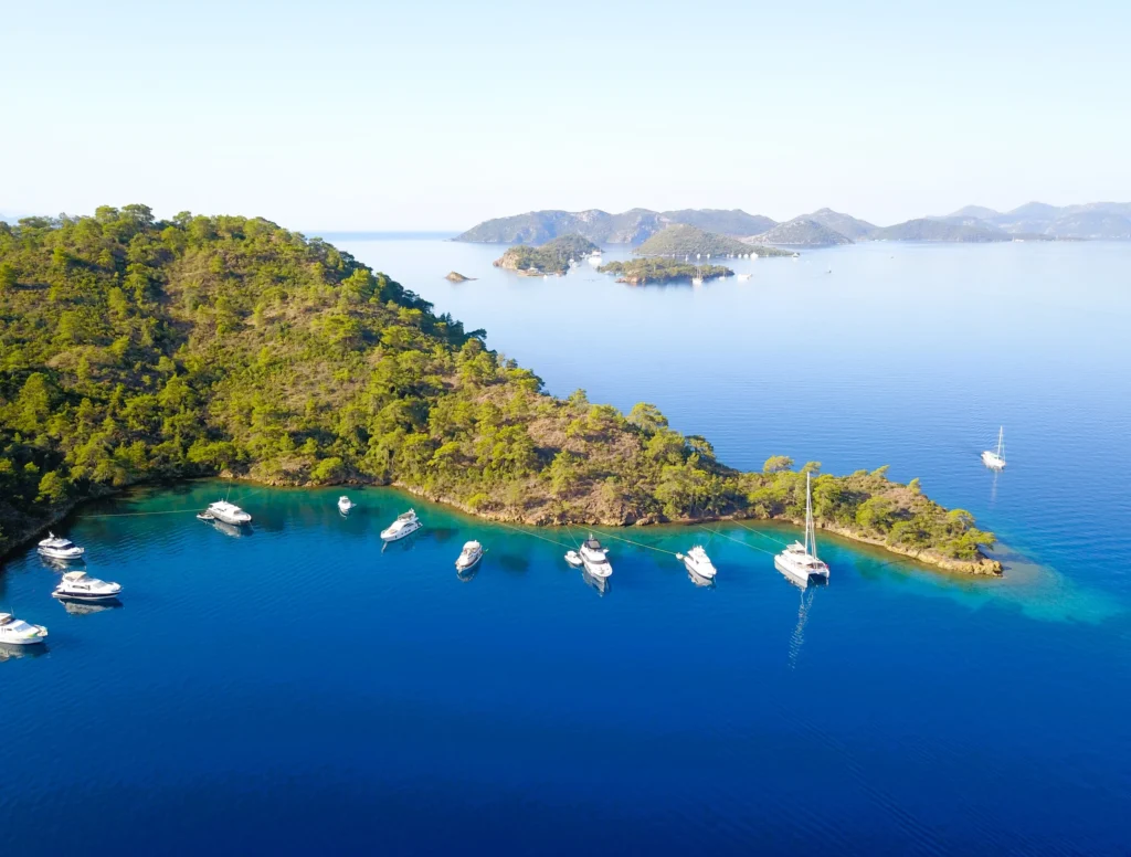 Luxury yacht cruising near Fethiye, Turkey, with crystal-clear turquoise waters, rugged coastline, and a charming marina.