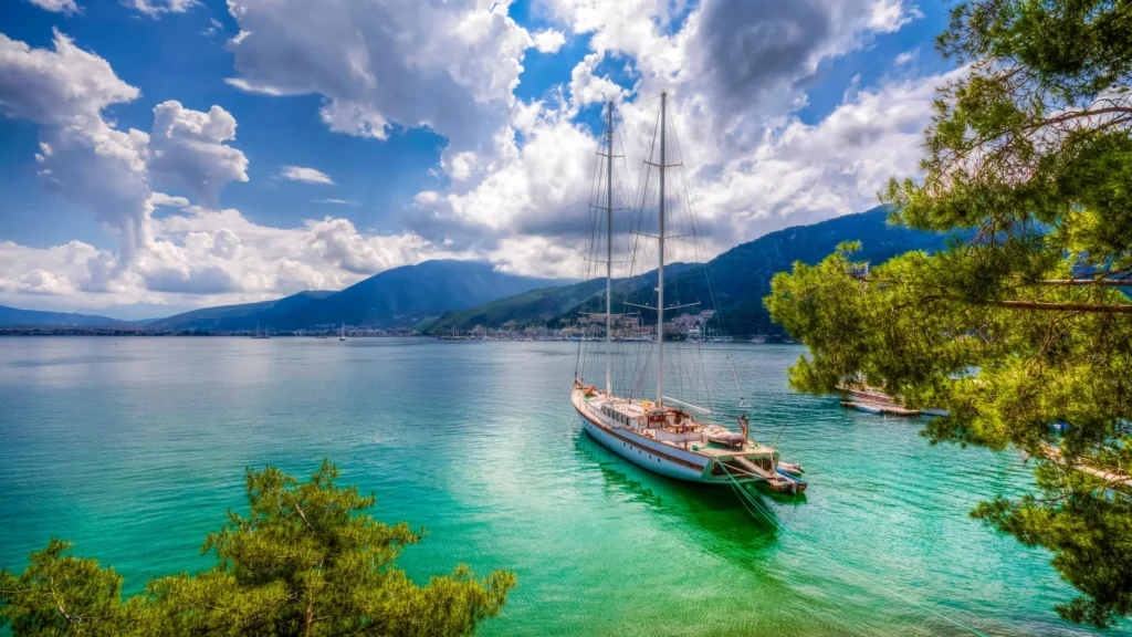 Luxury yacht cruising near Fethiye, Turkey, with crystal-clear turquoise waters, rugged coastline, and a charming marina.