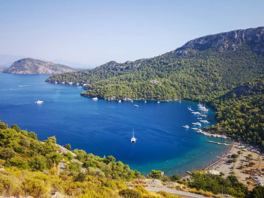 Luxury yacht cruising near Göcek, Turkey, with serene turquoise waters, rugged coastline, and a picturesque marina.