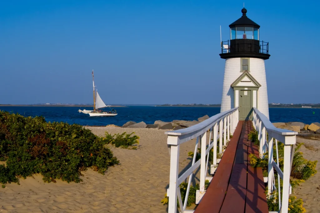 Luxury yacht anchored in Nantucket Harbor, Massachusetts, with classic sailboats, a historic lighthouse, and a charming New England coastline in the background