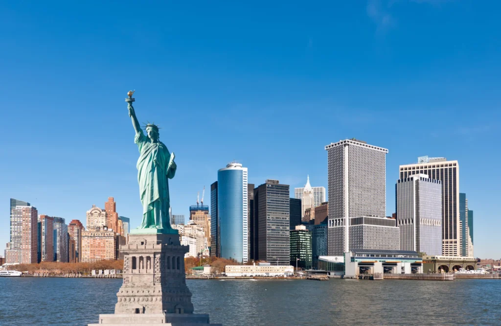 Luxury yacht cruising past the Manhattan skyline in New York City, with the Statue of Liberty and iconic skyscrapers in the background