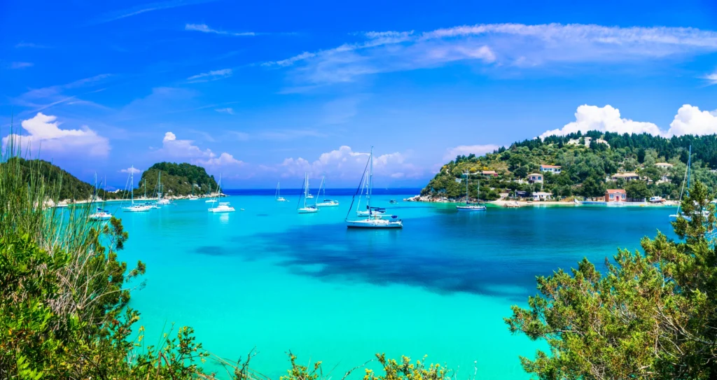 Luxury yacht cruising near Paxos, Greece, with crystal-clear Ionian Sea waters, lush landscapes, and charming island scenery with distant views of Corfu.
