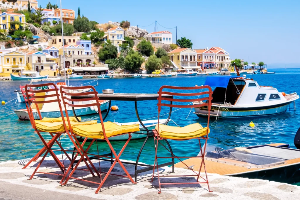 Luxury yacht cruising near Symi with clear turquoise waters, pastel-colored houses, and scenic harbor views in the Dodecanese Islands, Greece.