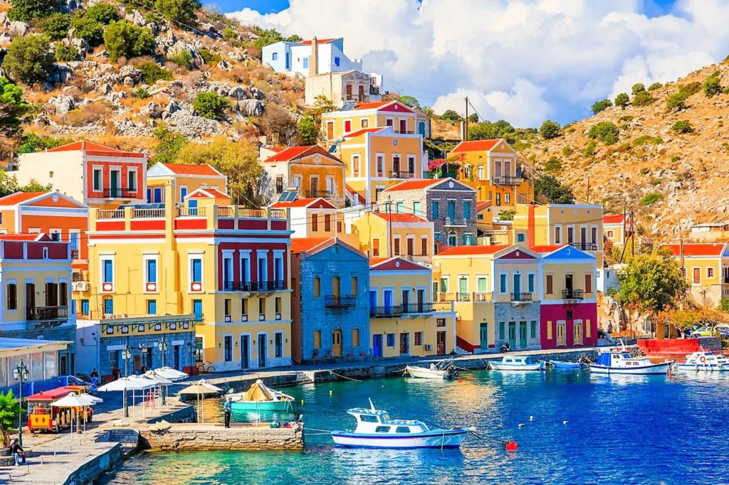 Luxury yacht cruising near Symi with clear turquoise waters, pastel-colored houses, and scenic harbor views in the Dodecanese Islands, Greece.