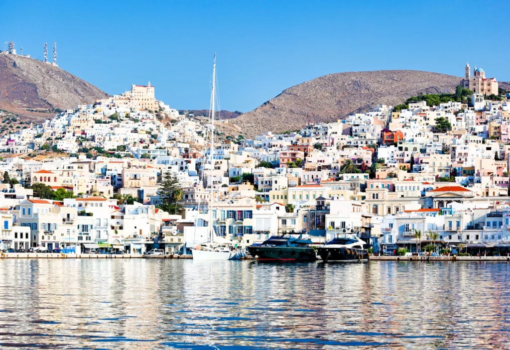 Luxury yacht cruising near Syros in the Cyclades Islands, Greece, with sparkling blue waters, charming neoclassical architecture, and scenic coastal views.