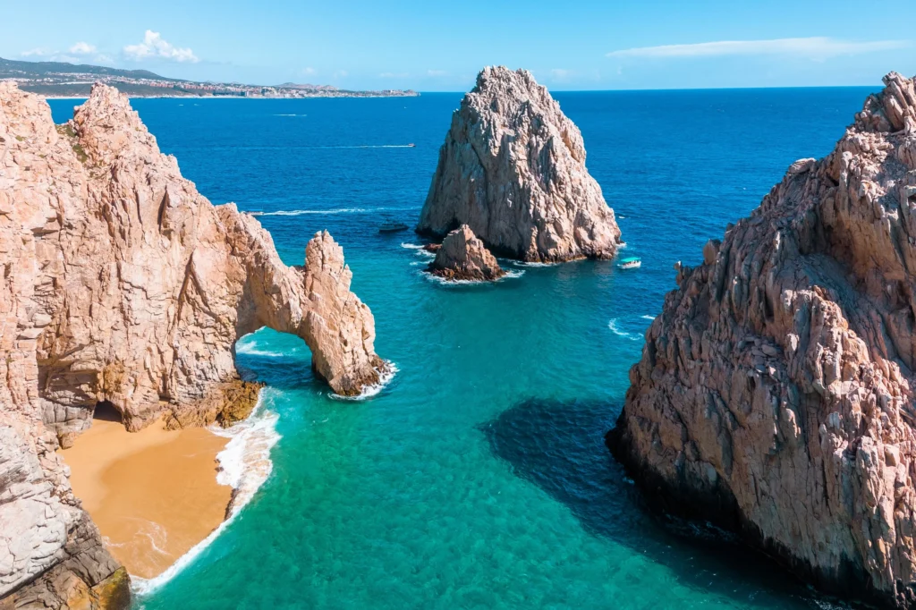 Luxury yacht sailing near the iconic Arch of Cabo San Lucas, Mexico, with rocky cliffs and blue ocean