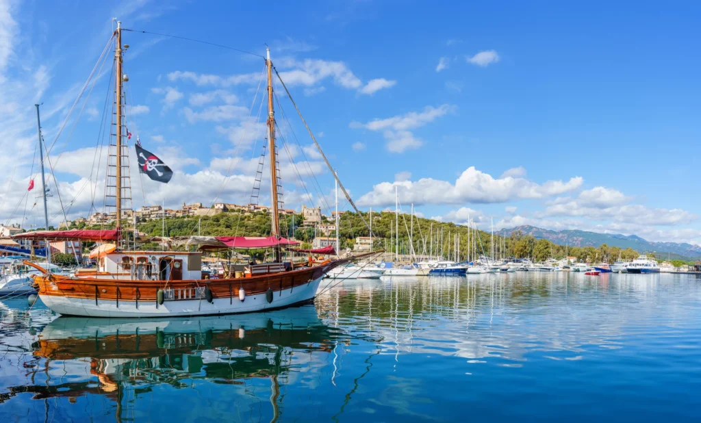 Luxury yacht cruising near Porto Vecchio, Corsica, with sparkling Mediterranean waters, scenic coastal cliffs, and a charming marina backdrop