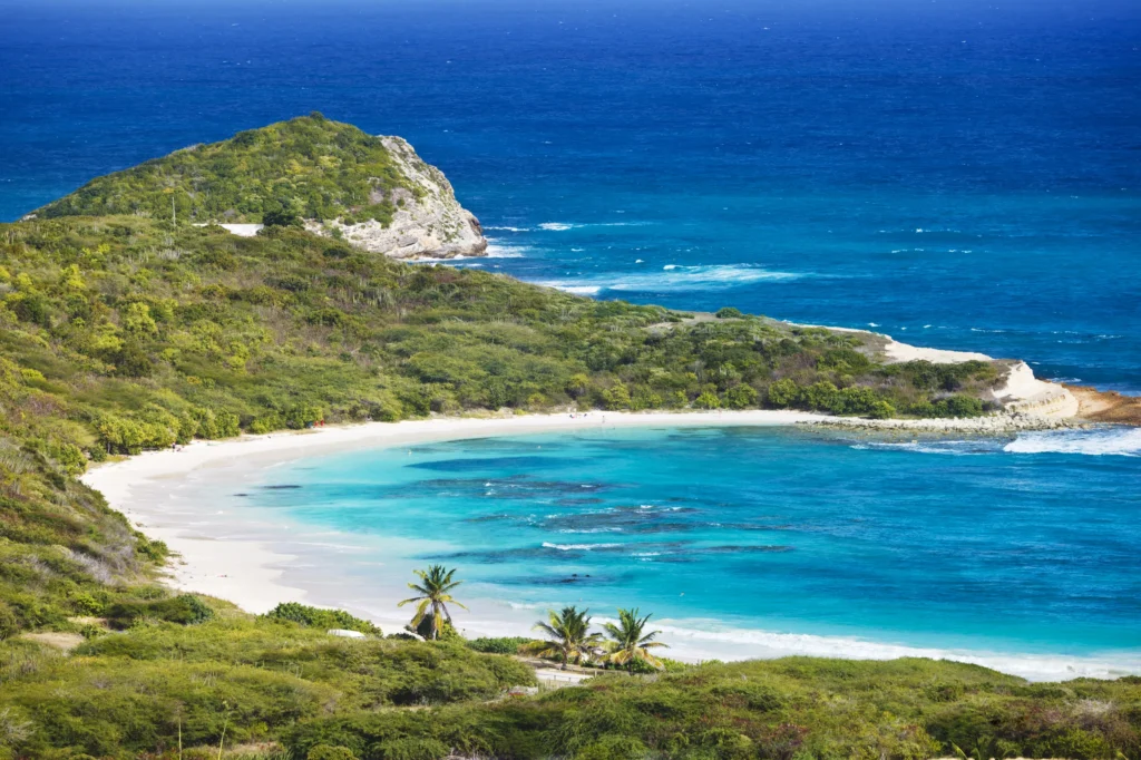 Luxury yacht cruising near Antigua in the Caribbean, featuring crystal-clear blue waters, lush tropical islands, and vibrant coastal scenery.