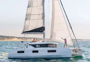Bareboat yacht under sail with guests at the helm, open teak deck, and clear blue sea—no crew on board.