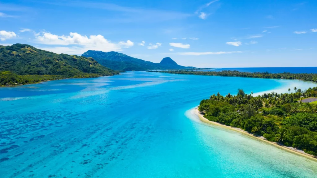 Luxury yacht anchored near Huahine, French Polynesia, with lush jungle-covered hills, calm blue lagoons, and remote sandy shores.