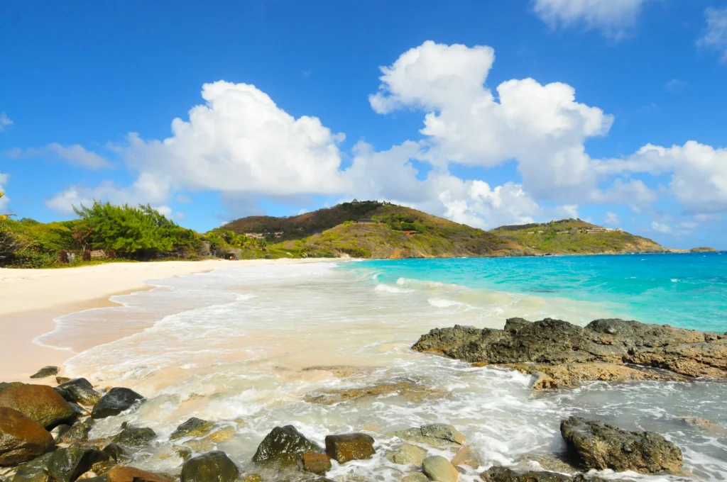 Luxury yacht anchored near Mustique in the Grenadines, with turquoise waters, lush hills, and elegant beachfront villas.