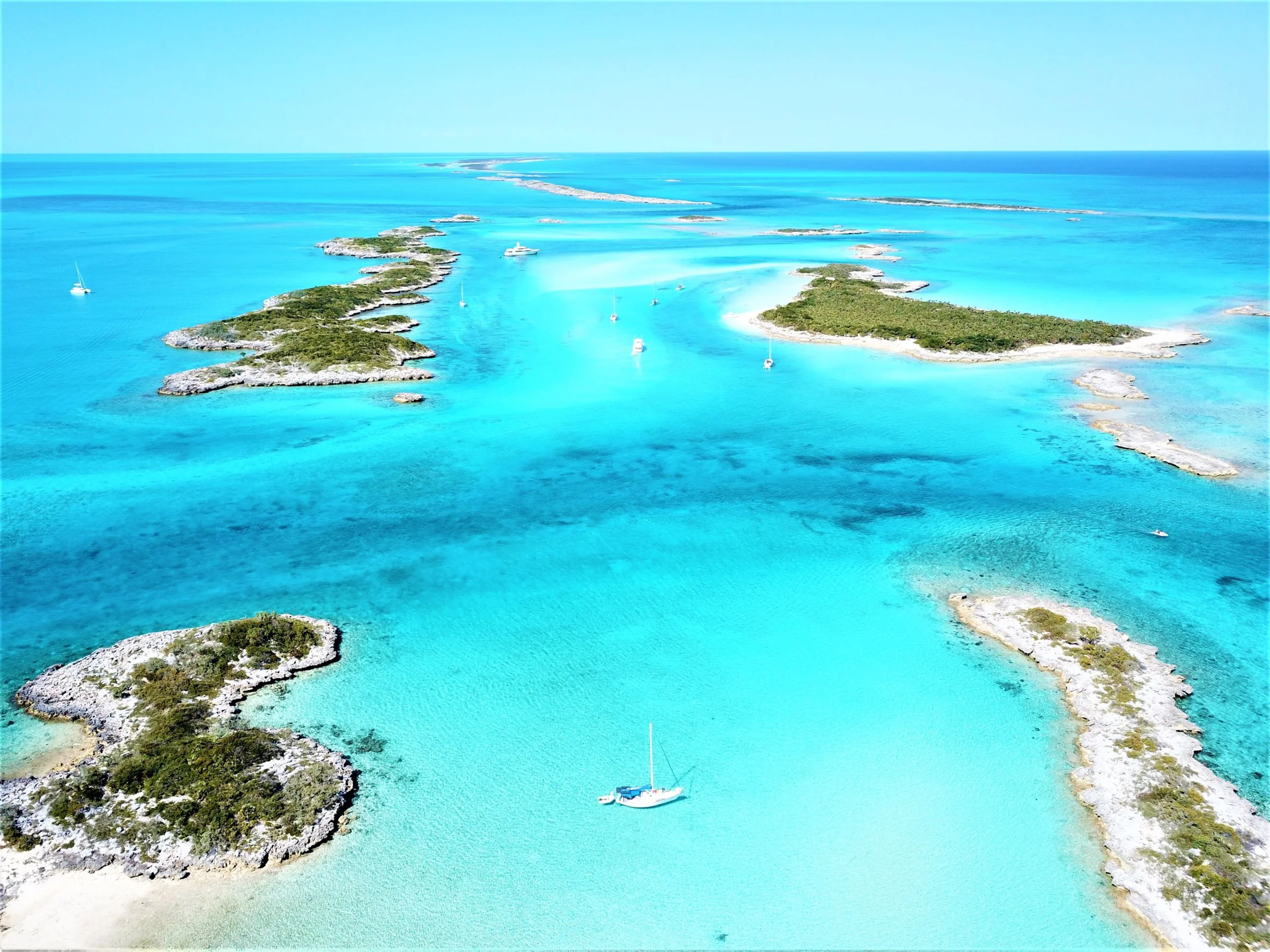 A luxury yacht anchored in the turquoise shallows of the Exumas, Bahamas, surrounded by sandbars and crystal-clear water.